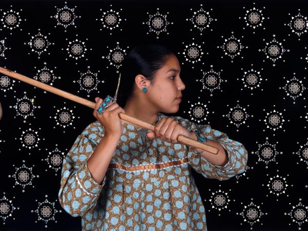 Photograph of a young Indigenous woman holding a stick